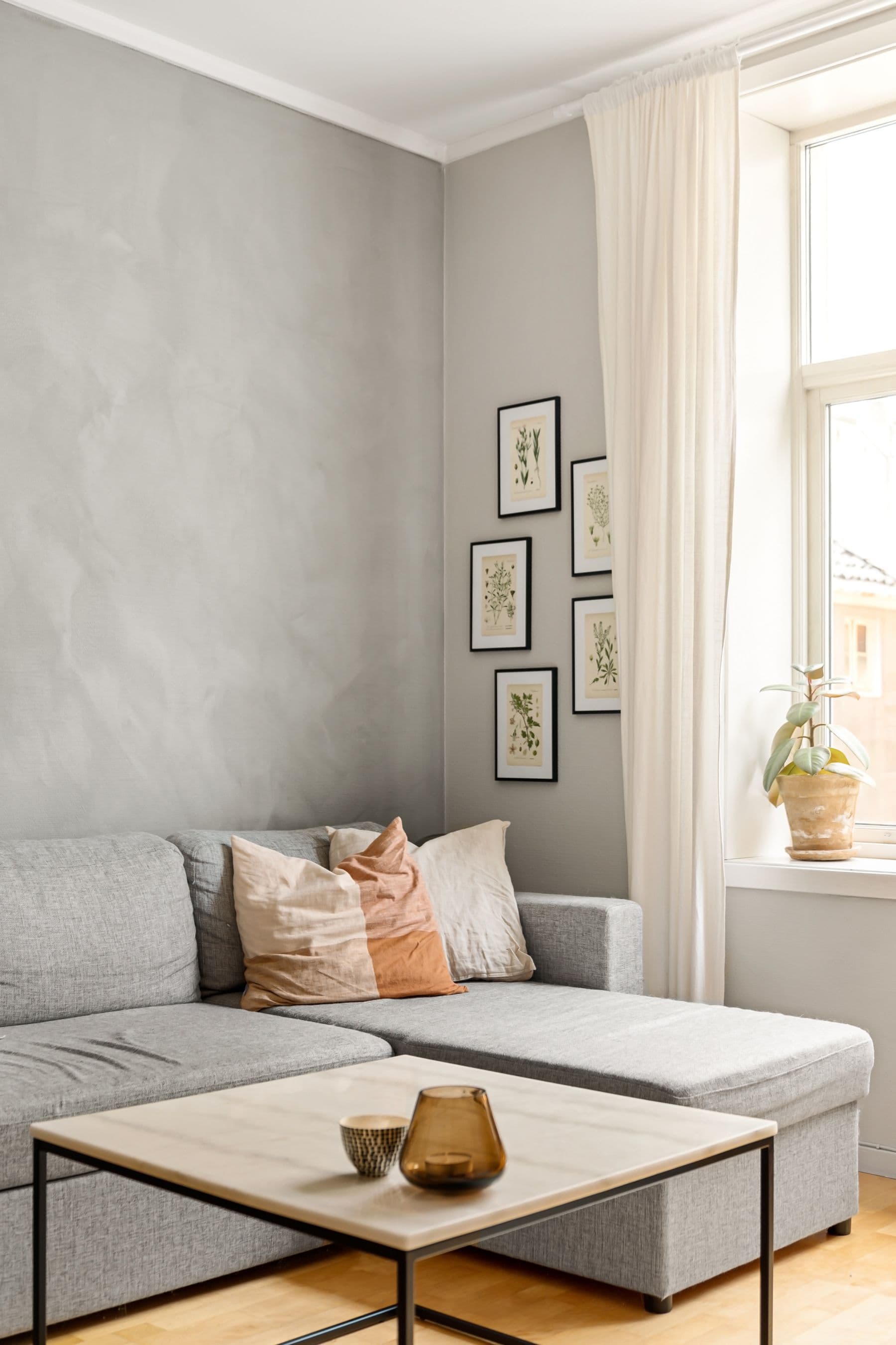 Sanft verputzte graue Wand über einem hellen Sofa mit Leinenkissen.