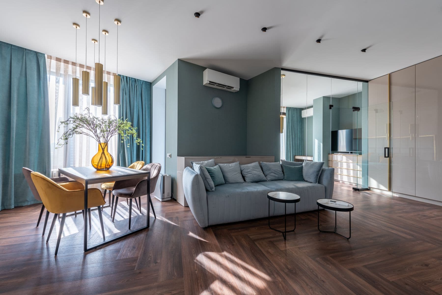 Modernes Wohnzimmer mit salbeifarbener Wand, grauem Sofa und warmem Holzboden.